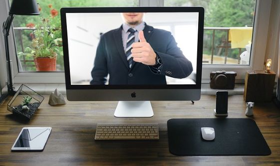 Escritorio con ordenador, mostrando un hombre en la pantalla del ordenador.